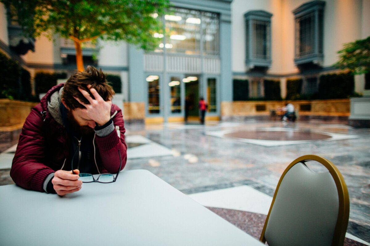 Man holding eyeglasses in hand, showing stress in a modern indoor atrium.